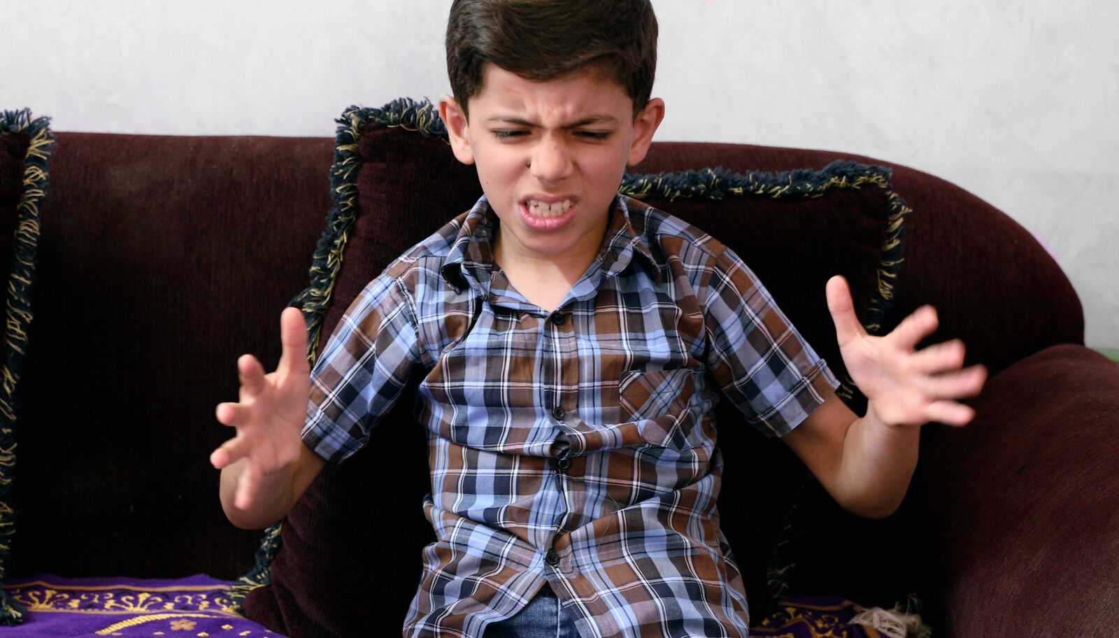 A boy in a plaid shirt gestures emphatically with both hands, his face full of feeling.